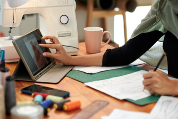 Hands of fashion designer zooming image of dress on tablet screen