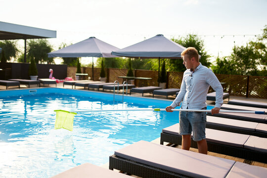 Man with skimmer net equipment cleaning swimming pool from rubbish. Service and maintenance of the pool. Male removes garbage from the water with a sap. Swimming pool cleaning service. Hotel cleaner.