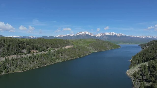 Aerial view over the lake surrounded by forest, snowy mountain range of Colorado Mountains.