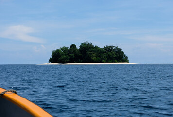 A tiny remote tropical island with white sandy beach, green trees and ocean views from boat in the Solomon Islands