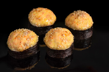 Baked sushi rolls with cheese on a black background with reflection.