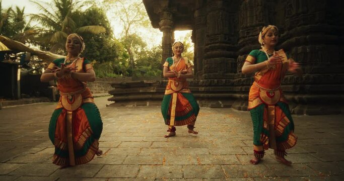 Slow Motion Portrait of Three Expressive Young Indian Dancers Performing Folk Dance Choreography in an Ancient Temple. Women in Traditional Clothes Dancing Bharatanatyam in Colourful Sari