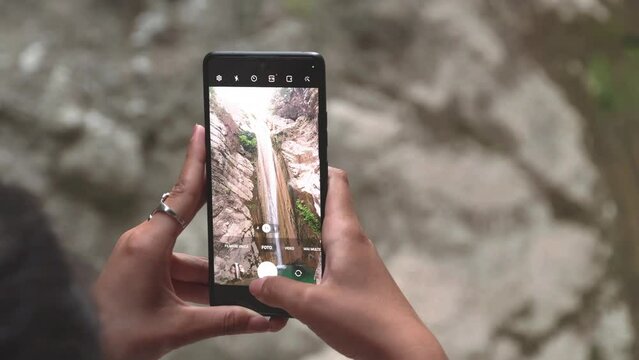 Young woman holding a phone and taking pictures of Nydri waterfall. Slow motion of woman hands holding a phone and taking pictures of waterfall