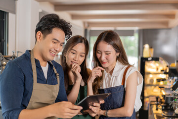 Three barista entrepreneur team meeting at coffee shop. Young smiling Asian male and female cafe employees having discussion on work and menu with tablet computer - 632085312
