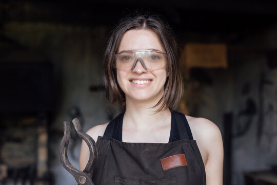 Young woman blacksmith portraitin protective glasses in workshop