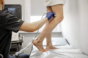 Ultrasound specialist is scanning the veins on a woman's leg, examining veins for varicose treatment - obrazy, fototapety, plakaty