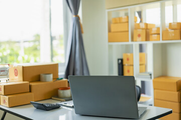 Delivery business, desk with laptop, parcel box, dispenser, packing tape and adhesive tape in warehouseBusiness ideaSME