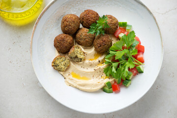 Falafel with hummus, chopped vegetables and fresh greens in a beige plate, horizontal shot, top view