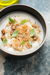 Bowl of cauliflower cream-soup topped with roasted florets and croutons, vertical shot on a grey granite background, middle closeup