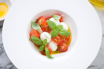 Middle close-up of caprese salad with baby mozzarella, cherry tomatoes, olive oil and green basil served in a white plate