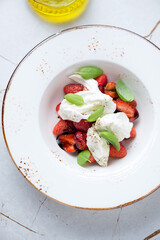 Mozzarella with balsamic strawberry and green basil in a beige plate, vertical shot on a white granite background, above view