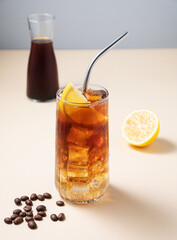 Coffee cold brew with tonic in a tall glass with ice and lemon on a yellow background with coffee beans,  bottle, fruits and fruits. Trendy summer craft refreshing drink.
