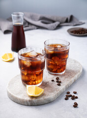 Cold brew coffee in a two glasses with lemon and ice on a marble board on a light background with coffee beans, bottle and napkin. Concept summer craft refreshing homemade drink