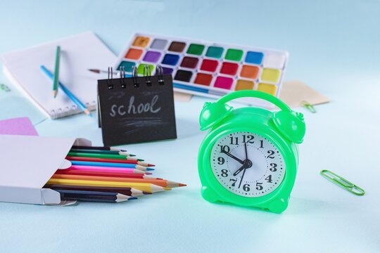School supplies and an alarm clock on a light blue background. Back to school concept.