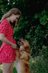 A young girl with long fair hair in a red jumpsuit hugs, strokes and plays with her dog.
- 632094554