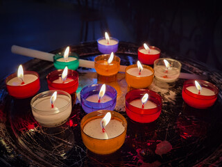 Algumas velas de diferentes cores a arderem no interior escuro de uma Igreja
