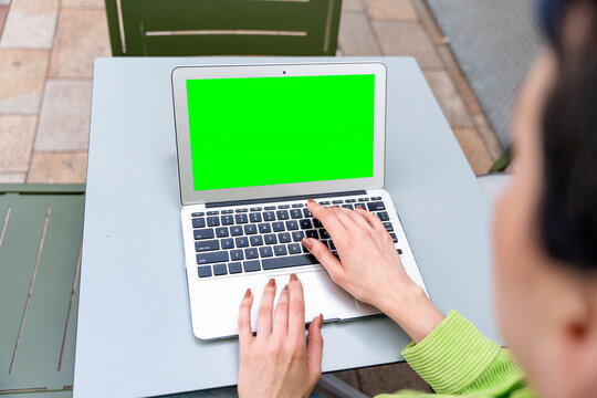woman having coffee at the street cafe outside, talking on the laptop with green screen and having fun time. lifestyle concept