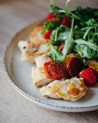 Fried chicken fillet and fresh vegetable salad of tomatoes and arugula leaves.