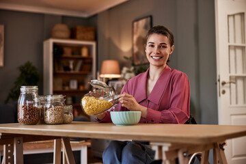 Portrait of a smiling woman in a wheelchair making a bowl of cereal for breakfast at home.