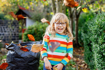 Little preschool girl working with rake in autumn garden. Adorable happy healthy child having fun...