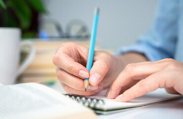 A young girl student prepares her homework and writes notes in a notebook. Close-up. Selective focus.