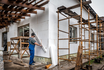 Insulation of the house with polyfoam. The worker is checking with the construction level the accuracy of the installation of polystyrene board on the facade