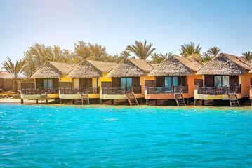Row of wooden bungalows with straw roof in sea water