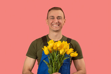 Delivery man with beautiful smile holds bouquet of yellow flowers, pink background. Flowers delivery concept.