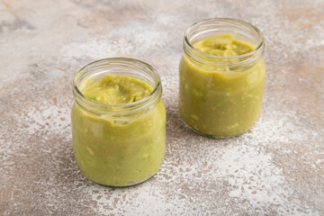 Baby puree with vegetable mix, broccoli, avocado in glass jar on brown concrete, side view