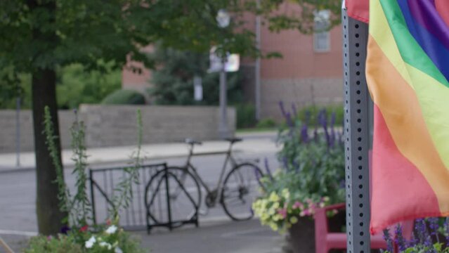 Rainbow pride flag waving in the wind in Lansing, Michigan Old Town district with stable establishing shot.