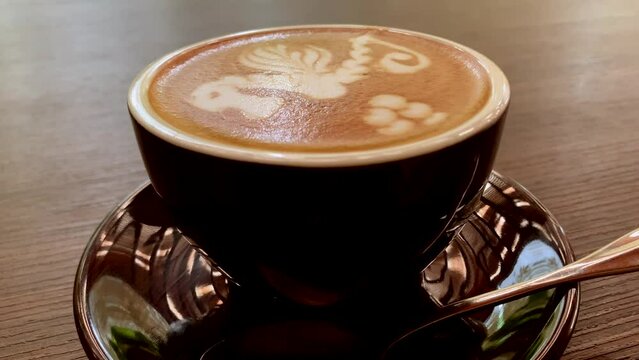 A cup of cafe latte with beautifully drawn horse art on the top was placed on the table with a teaspoon on the side.