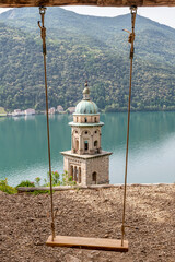 Fototapeta na wymiar The bell tower of the church of Santa Maria del Sasso in Morcote, Switzerland, framed by the ropes of a high swing