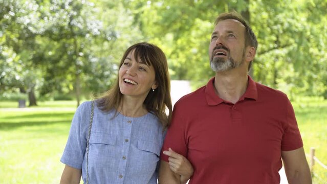 A Middle-aged Caucasian Couple Points At Something Off The Camera And Smiles As They Walk In A Park