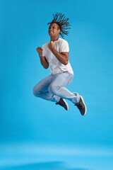 Fototapeta premium Reaching success. Full-length image of young man in casual clothes jumping with happy emotions against blue studio background. Concept of youth, human emotions, lifestyle, fashion, ad