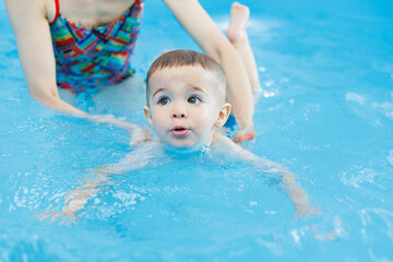 Fototapeta na wymiar A 2-year-old boy learns to swim in a pool with a coach. Swimming lessons for children. Swimming school for children. Educational swimming courses for children