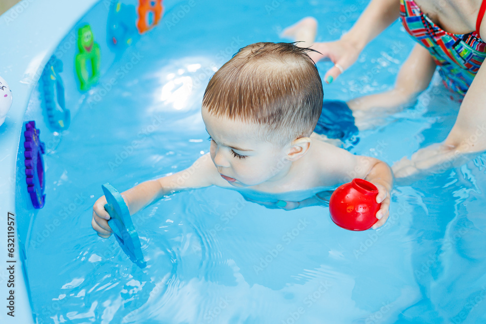 Wall mural a 2-year-old little boy is learning to swim in the pool. swimming lessons for young children. swimmi