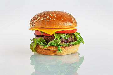 home cooked burger with cheese, tomatoes, chard and arugula on a white glass surface