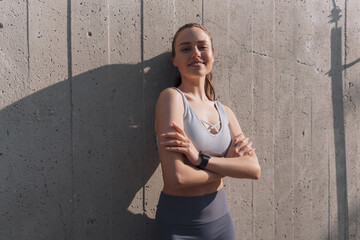 Portrait of young sporty woman standing in front of concrete wall in the city.