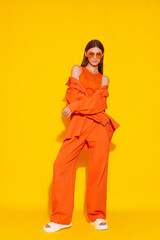 Young fashion woman in orange pants orange top orange shirt on yellow background. Platform slides...