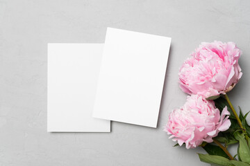 Fototapeta premium Wedding invitation card mockup with pink fresh peony flowers, blank card mock up on grey background, top view with copy space