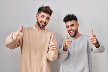 Young homosexual couple standing over white background pointing fingers to camera with happy and funny face. good energy and vibes.