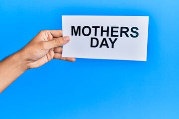 Hand of caucasian man holding paper with mothers day message over isolated blue background