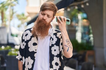 Young redhead man listening audio message by sthe smartphone at street