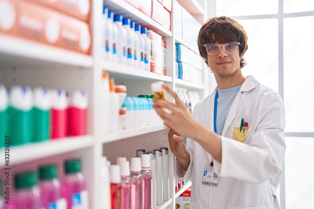 Wall mural Young blond man pharmacist holding pills bottle at pharmacy