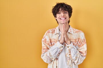 Young man wearing casual summer shirt praying with hands together asking for forgiveness smiling...