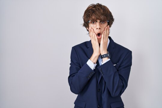 Hispanic business young man wearing glasses afraid and shocked, surprise and amazed expression with hands on face