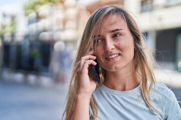 Young blonde woman smiling confident talking on the smartphone at street