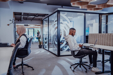Fototapeta na wymiar In a modern office setting, an African American businessman and his Muslim colleague, wearing a hijab, engage in collaborative discussions, tackling various business tasks and solving problems