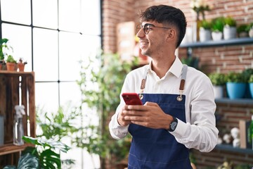 Young hispanic man florist smiling confident using smartphone at florist