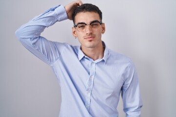 Handsome hispanic man wearing business clothes and glasses confuse and wonder about question. uncertain with doubt, thinking with hand on head. pensive concept.
